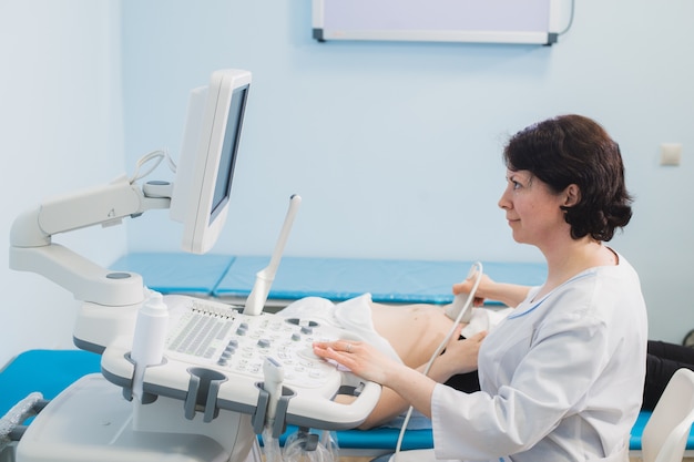 Doctor using ultrasound and screening of stomach of pregnant woman.