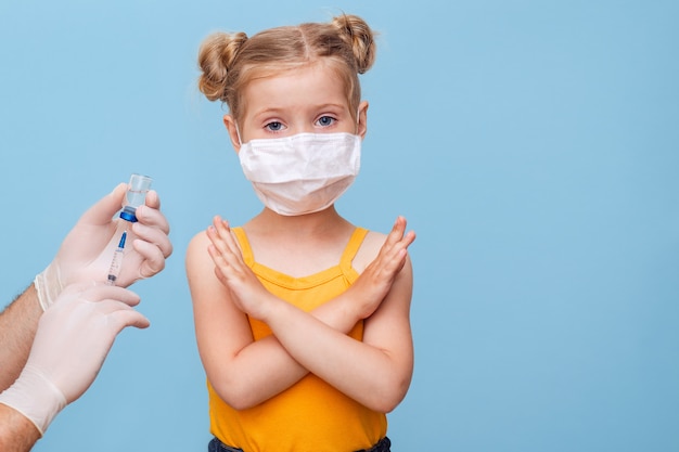 A doctor vaccinates a little blonde girl in a medical mask