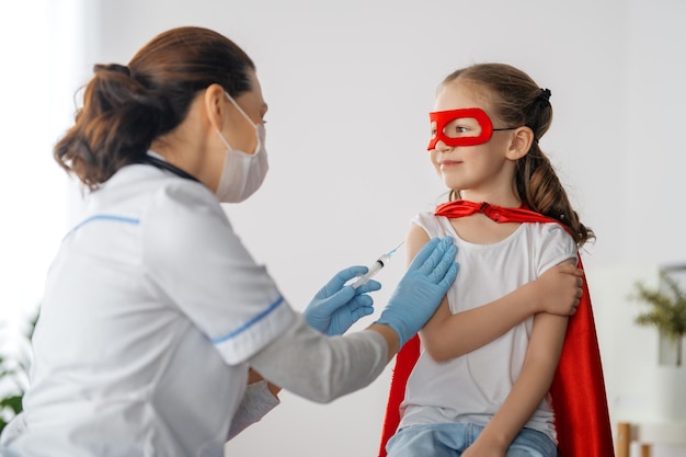 Doctor vaccinating child at hospital kid in superhero\
costume