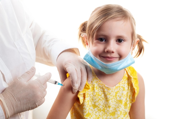 Medico che vaccina la bambina sorridente sveglia che porta vestito giallo e maschera protettiva per il viso