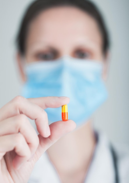 Doctor wearing blue face medical mask holding tablet pill on grey hospital wall background Antibiotics and virus treatment tablet