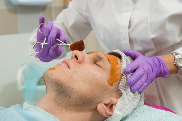 A doctor wearing gloves treats the face of a young male patient before undergoing cosmetic surgery