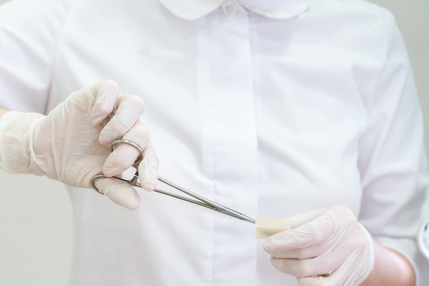 Doctor wearing gloves using a surgical forcepsto open band aid