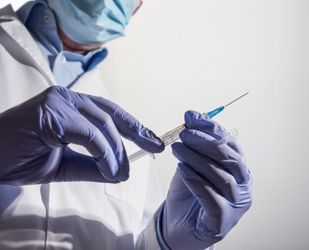 Doctor wearing mask and gloves holds a disposable syringe