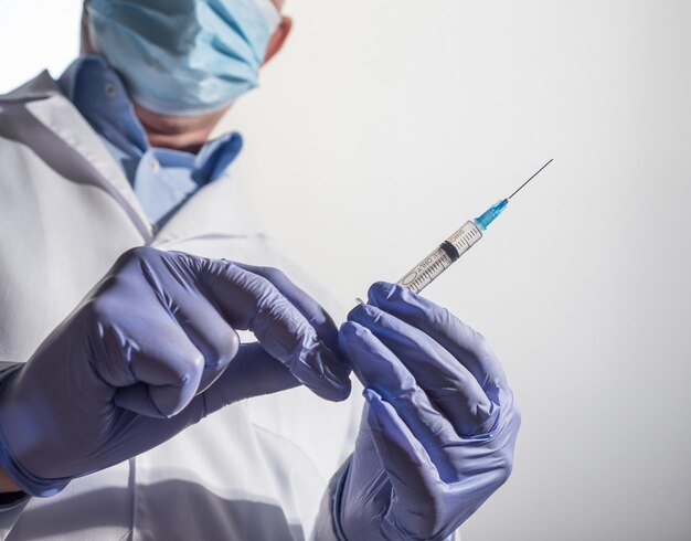 Doctor wearing mask and gloves holds a disposable syringe