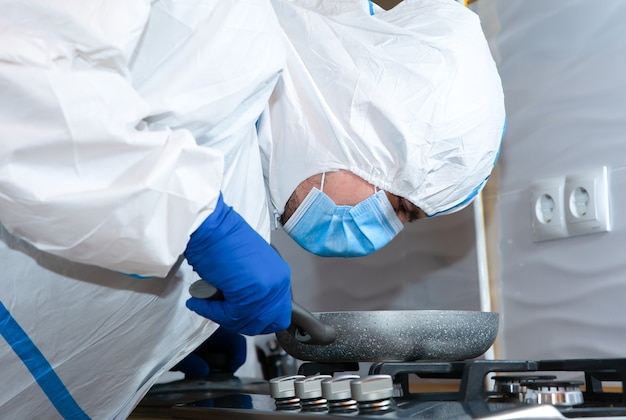 Medico che indossa tuta protettiva medica, occhiali, maschera e guanti che preparano il cibo. pentola sul fornello a gas. protezione dall'epidemia di virus. coronavirus (covid-19). concetto di assistenza sanitaria.