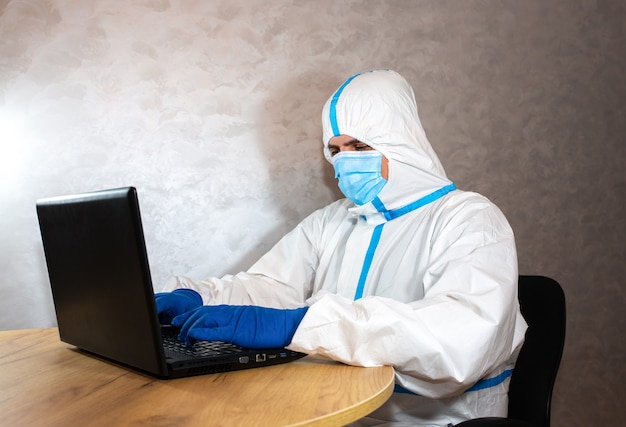 Doctor wearing medical protective suit, medical mask and gloves working on laptop. protection mers by virus epidemic. coronavirus (covid-19). healthcare concept. remote work in a pandemic covid