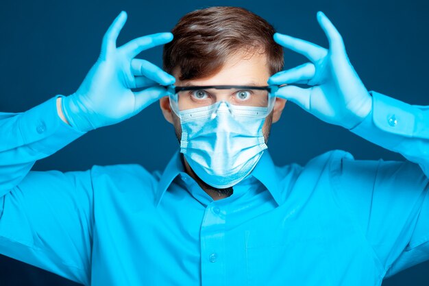 Doctor wearing a protective mask and gloves puts on medical glasses.