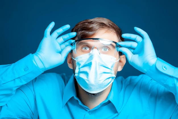 Doctor wearing a protective mask and gloves puts on medical glasses.