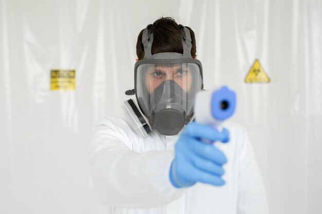 Medico che indossa una maschera protettiva pronto per l'uso del termometro a infrarossi sulla fronte per controllare la temperatura corporea per i sintomi del virus