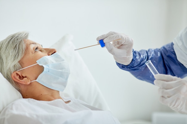 Доктор в защитной форме берет мазок из носа пожилой женщины для теста на коронавирус с помощью палки
