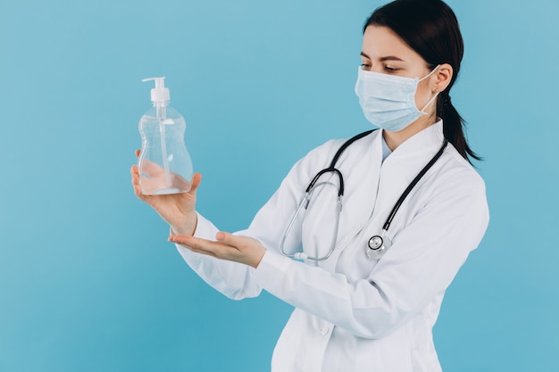 医師は、アルコールジェルポンプボトルを示す手術用マスクを身に着けています。アルコールジェルまたは抗菌石鹸消毒剤で手を洗う。 Covid-19またはコロナウイルスの概念。