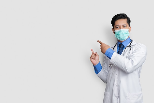 Photo doctor wearing uniform smiling while presenting and pointing isolated on white wall with copy space