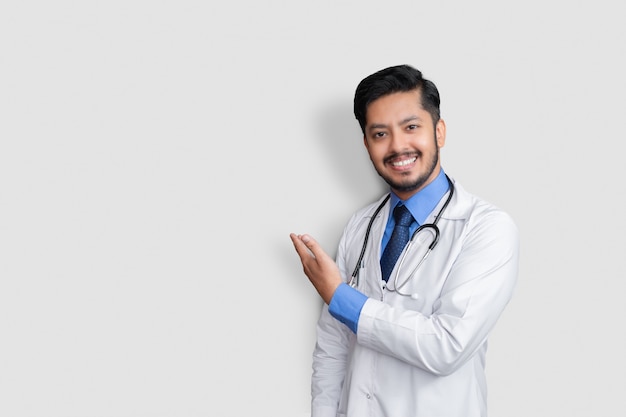 Photo doctor wearing uniform smiling while presenting and pointing isolated with copy space