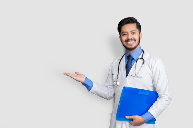 Doctor wearing uniform smiling while presenting with patient file in hand isolated on white wall with copy space