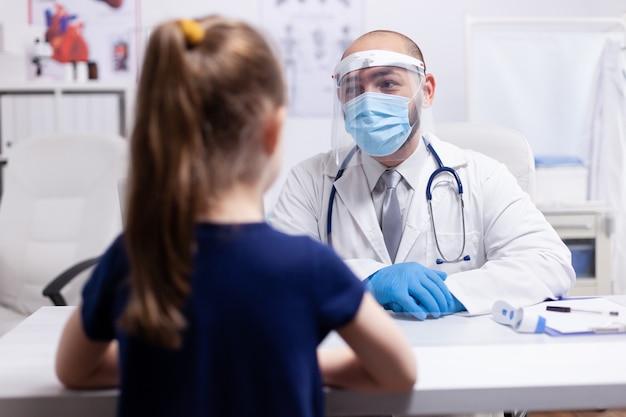 Doctor wearing visor for safty precaution during coronavirus while having child for examination