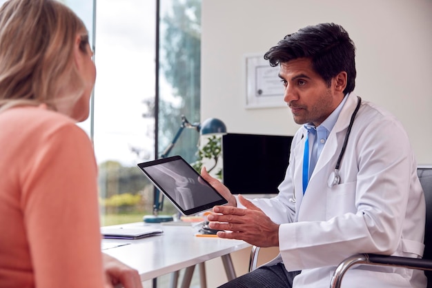 Доктор в белом халате в офисе показывает рентген или сканирование зрелой пациентки на цифровом планшете