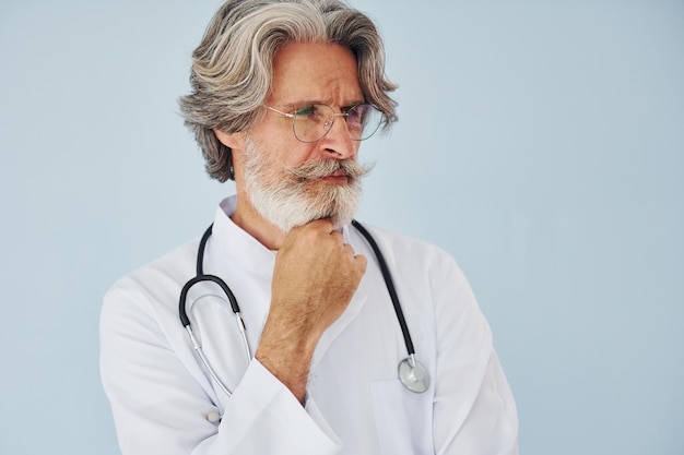 Doctor in white coat against wall Senior stylish modern man with grey hair and beard indoors