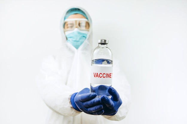 白いコートと青い手袋をした医師が、コロナウイルスワクチンが入った注射器の試験管を持っています。 Covid 2019ワクチン注射。 2020パンデミックコロナウイルス。ワクチンテスト。