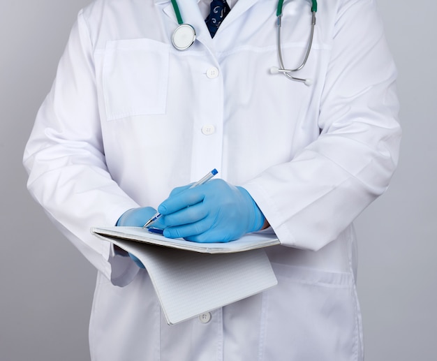 Doctor in a white coat, blue latex sterile gloves holds an open yellow notebook in his hand on a white background