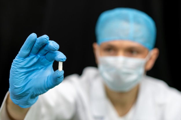 A doctor in a white coat holds a pill in his hand on a black background Medical preparations for the treatment of coronavirus A young intern doctor is considering a new drug