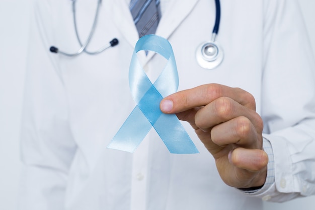 Doctor in a white coat is holding a blue ribbon