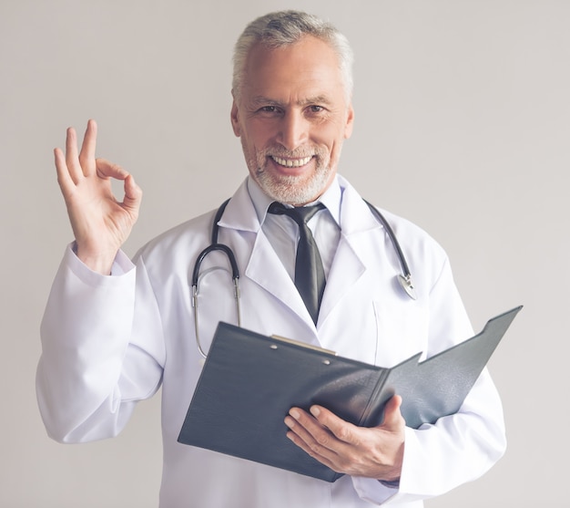 Doctor in white coat is holding a folder and showing Ok sign