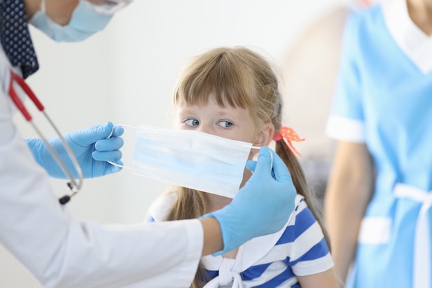 Doctor in white coat and with stethoscope puts on protective mask for child