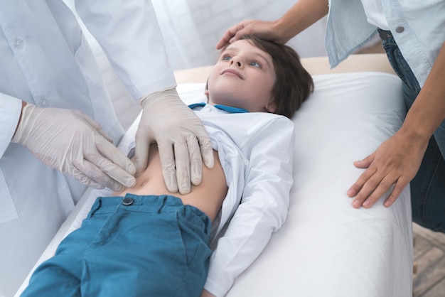 Photo the doctor in white gloves massages the belly of a sick boy.