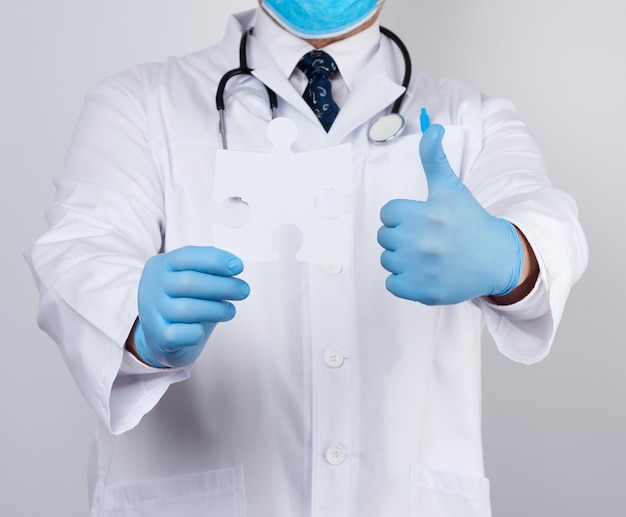 白い医療コートと青いゴム手袋の医師がホワイトペーパーパズルを保持しています。