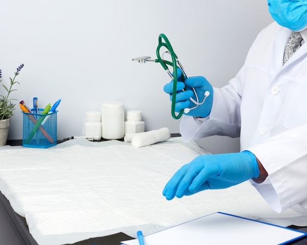 Doctor in a white medical coat sits at a table and holds a green stethoscope