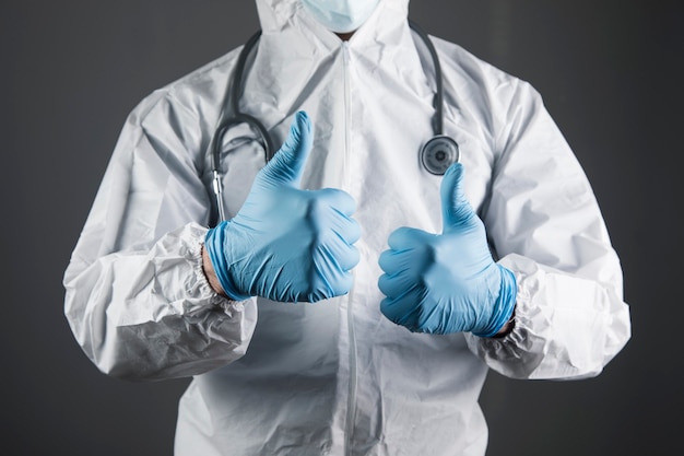 Doctor in white protective uniform shows thumb up on with gray scene