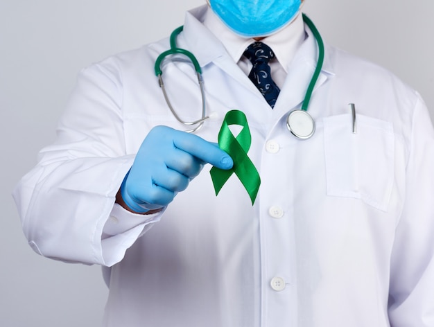 Doctor in white uniform and latex gloves holds a green ribbon