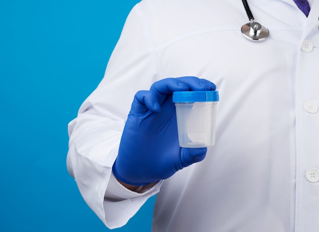 Doctor in white uniform and latex gloves is holding an empty plastic container for taking urine samples