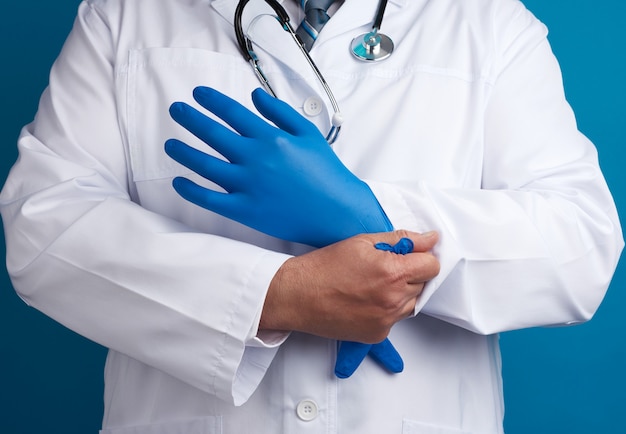 Doctor in white uniform puts on his hands blue sterile latex gloves