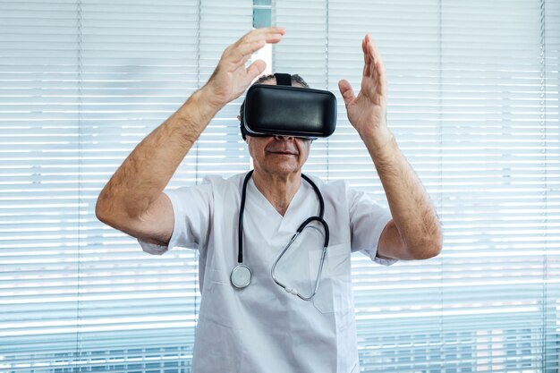 Doctor at the window of a hospital, using virtual reality glasses for medical purposes, touching something virtual with his hands