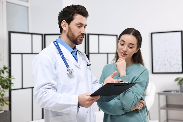 Doctor with clipboard consulting patient during appointment in clinic