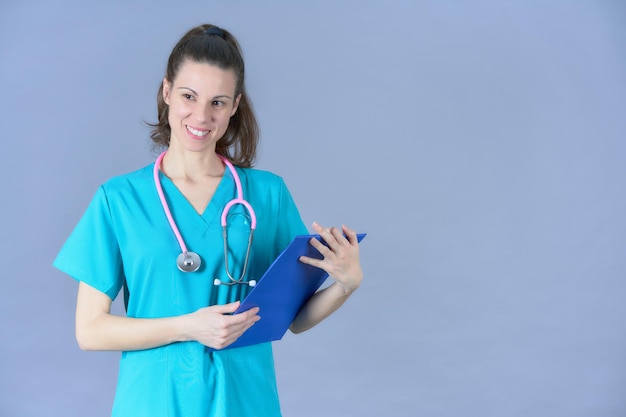 Doctor with clipboard and pink stethoscope frontally on blue background smiling brunette woman