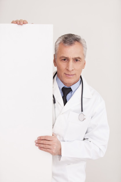 Doctor with copy space. Senior grey hair doctor in uniform looking out of copy space and smiling while isolated on white