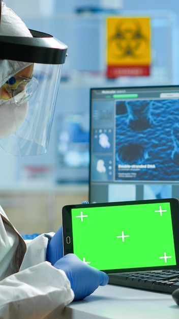 현대적인 시설을 갖춘 실험실에서 녹색 화면이 있는 태블릿에서 작업복을 입은 의사. 크로마 키, 격리된 모형 디스플레이가 있는 장치에서 백신 연구를 하는 미생물학자 팀.