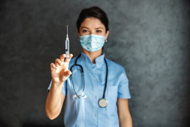 Foto medico con maschera per il viso che tiene la siringa con il vaccino. è importante essere vaccinati durante il virus corona. messa a fuoco selettiva a portata di mano.