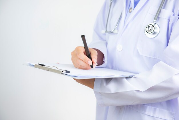 Doctor with files and stethoscope on hospital corridor holding clipboard and writing prescription