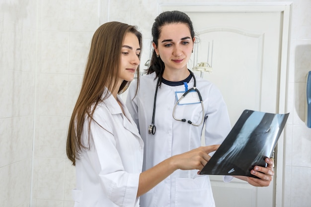 Doctor with intern examining patient's x-ray. Both wearing medical uniform and standing in hospital