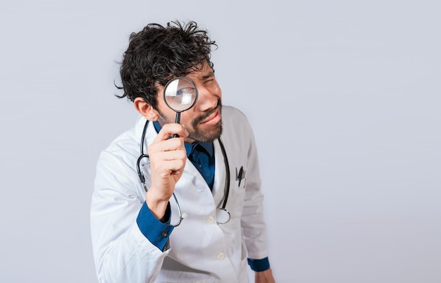 Doctor with magnifying glass looking at the camera Doctor holding magnifying glass and looking at camera on isolated background