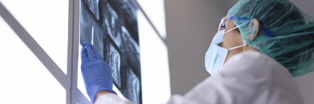 Doctor with medical mask in office examines an X-ray.