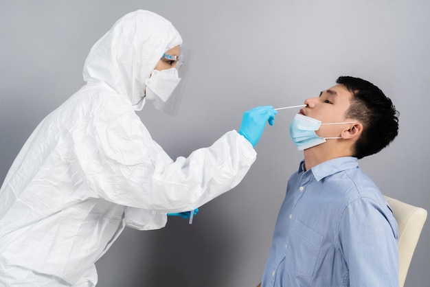 Врач в костюме СИЗ проверил молодого человека на коронавирус (covid-19) по мазку из носа