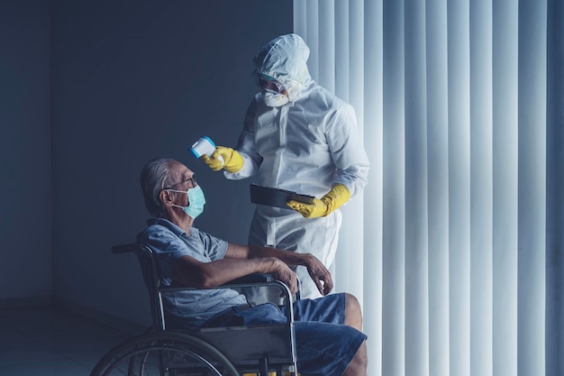 Doctor with protective suit measuring body temperature of an aged male patient