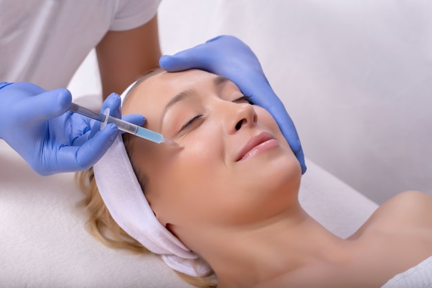 Doctor with rubber gloves doing a plastic face surgery on a happy young female