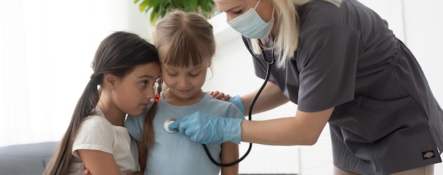 doctor with a stethoscope checks two little girls.