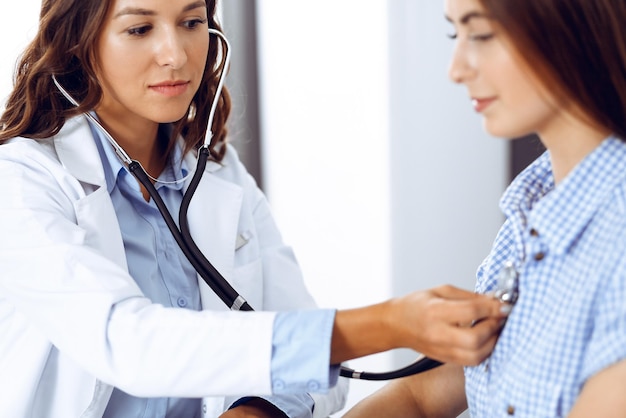 Foto medico con uno stetoscopio in mano che esamina la sua paziente. concetti di assistenza sanitaria, cardiologia e medicina.